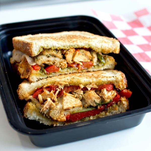 Two halves of a grilled chicken and roasted red pepper sandwich in a black to-go container.