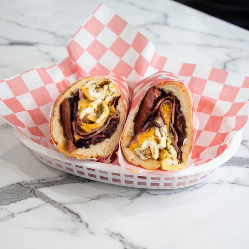 Two halves of a breakfast sandwich with eggs, cheese, and meat in a basket with checkered paper.